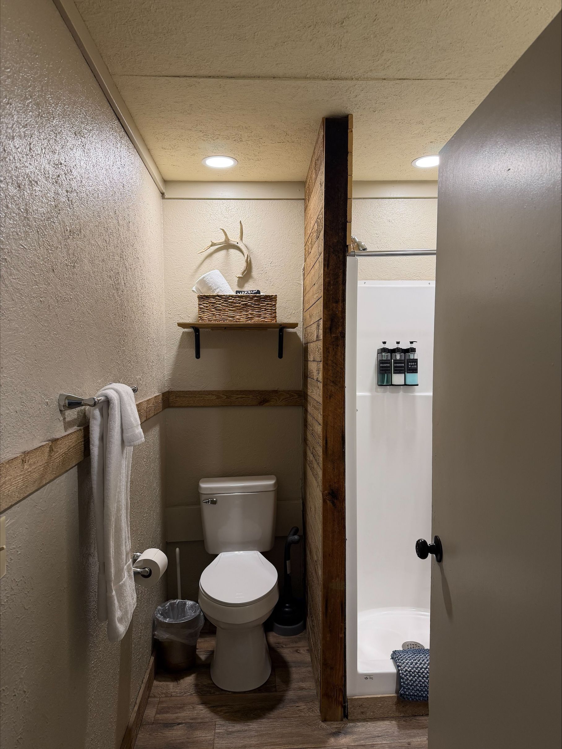 Narrow bathroom with toilet, towel rack, shelf, mirror, and shower stall in beige tones