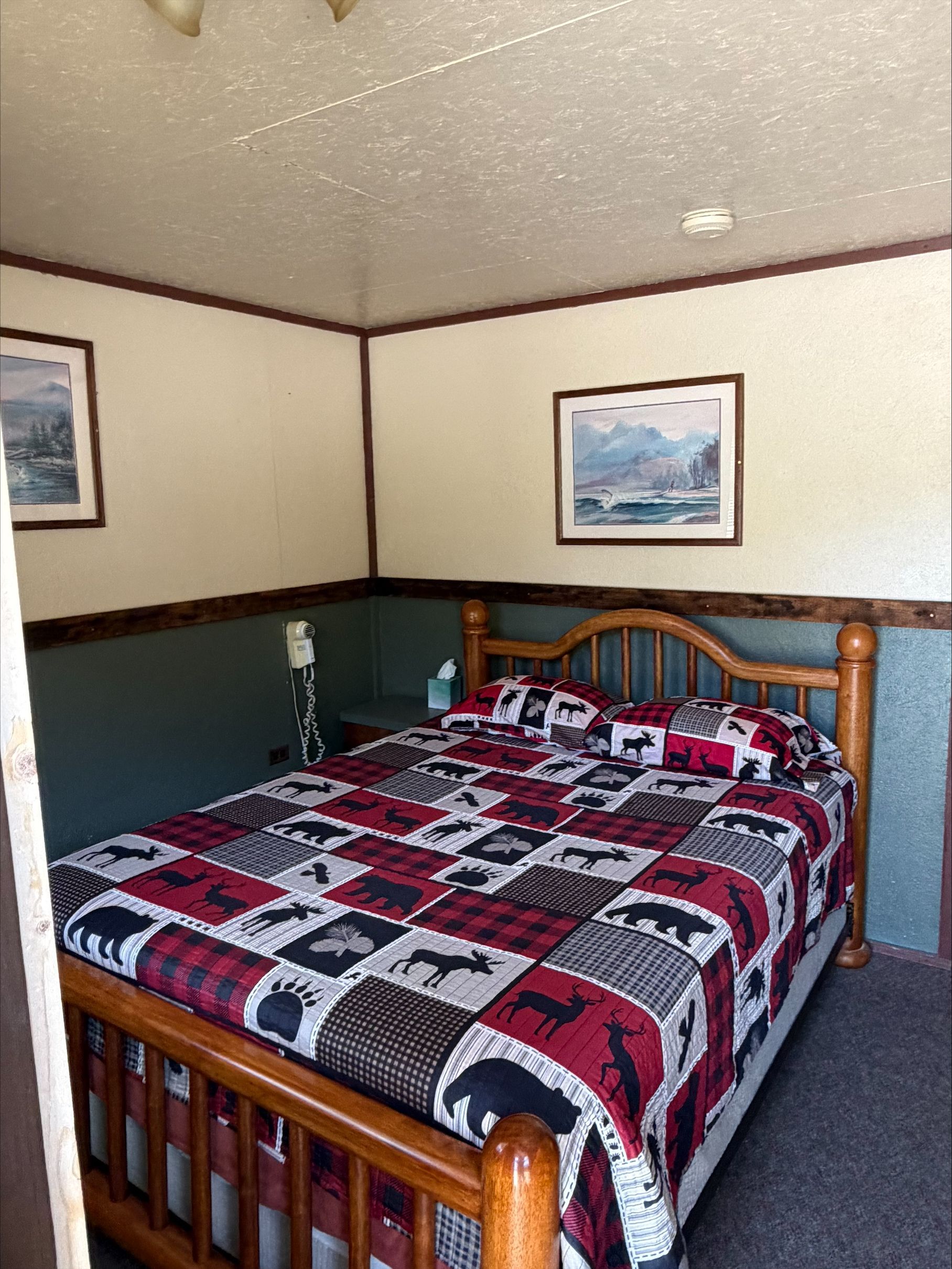 Wooden bed with red, black, and white patchwork quilt in a cozy bedroom with framed wall art.