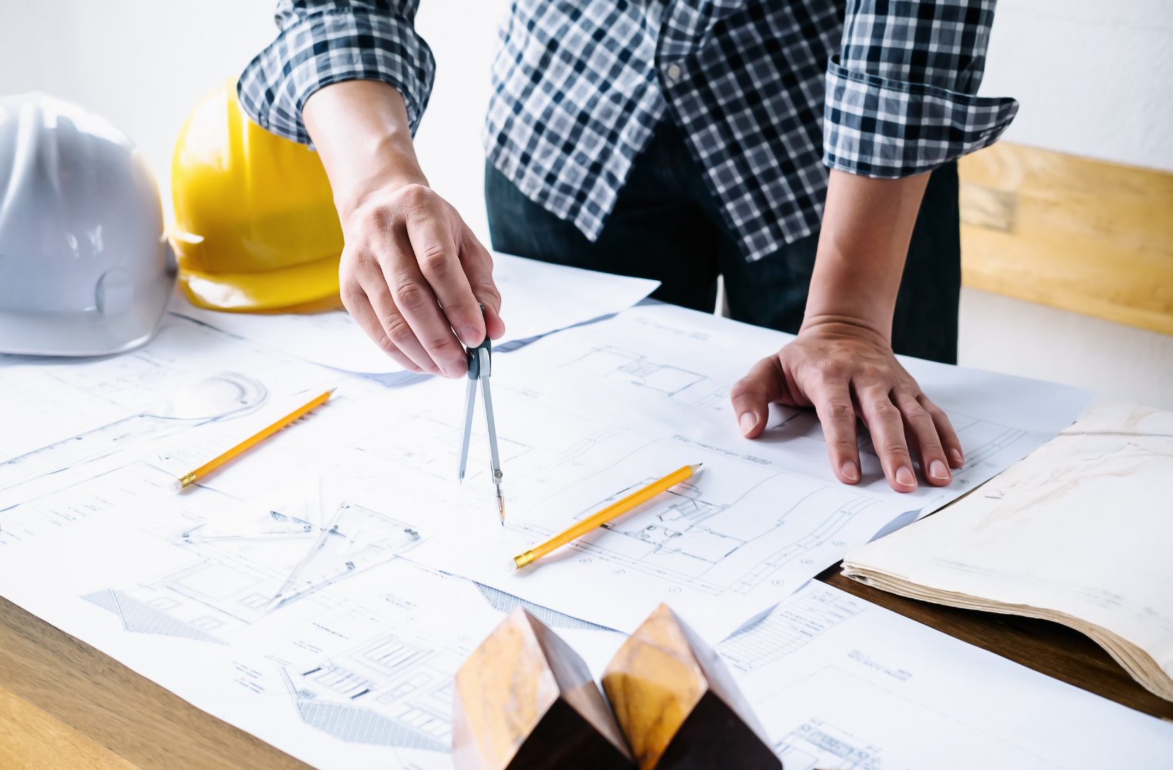 A man is using a compass to draw a house on a blueprint.