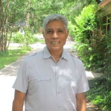 A man in a white shirt is standing on a sidewalk in front of trees.