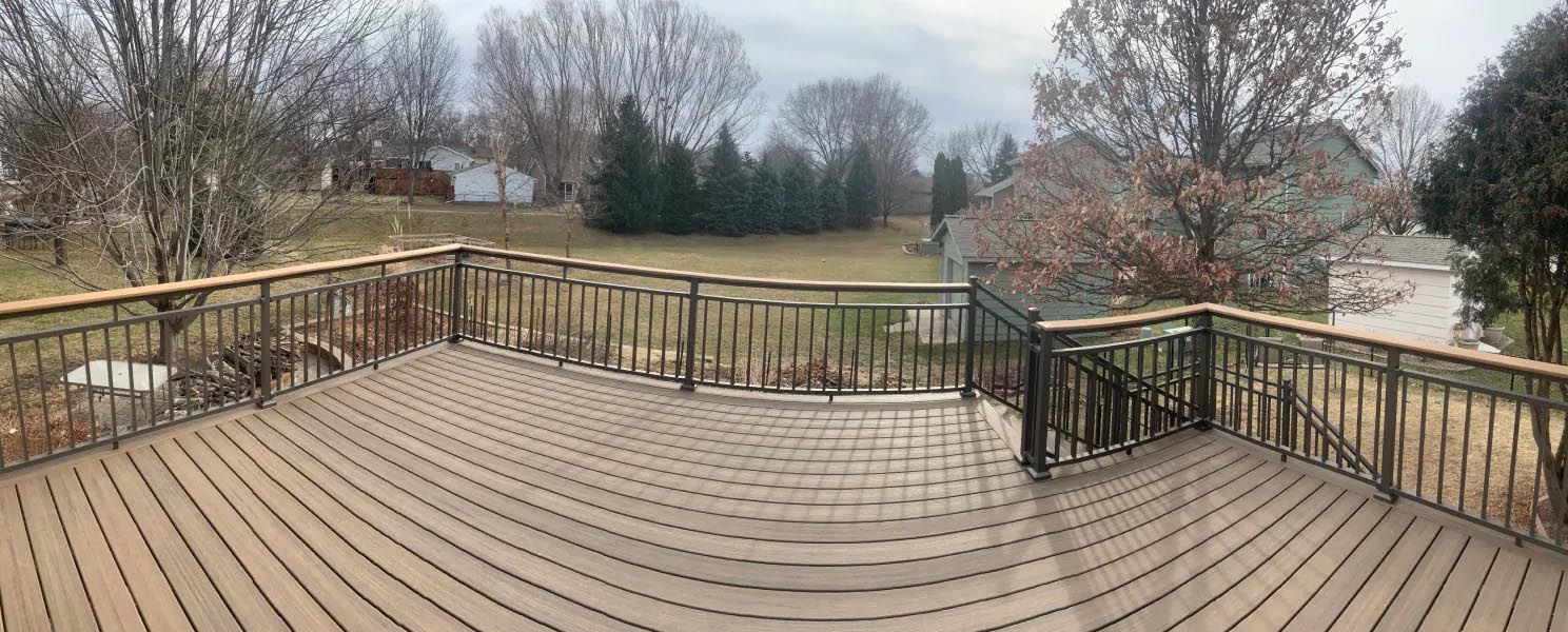 A large wooden deck with a metal railing and trees in the background.
