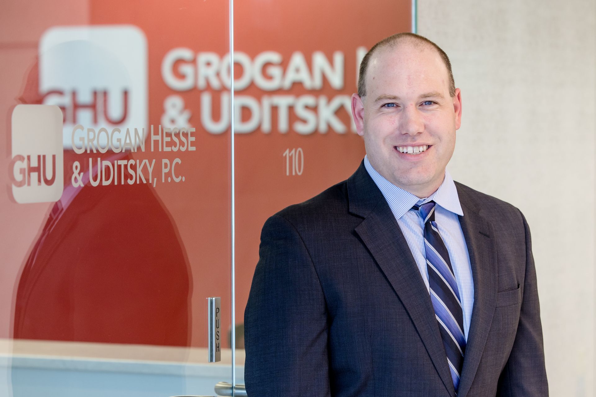 A man in a suit and tie is standing in front of a glass door.