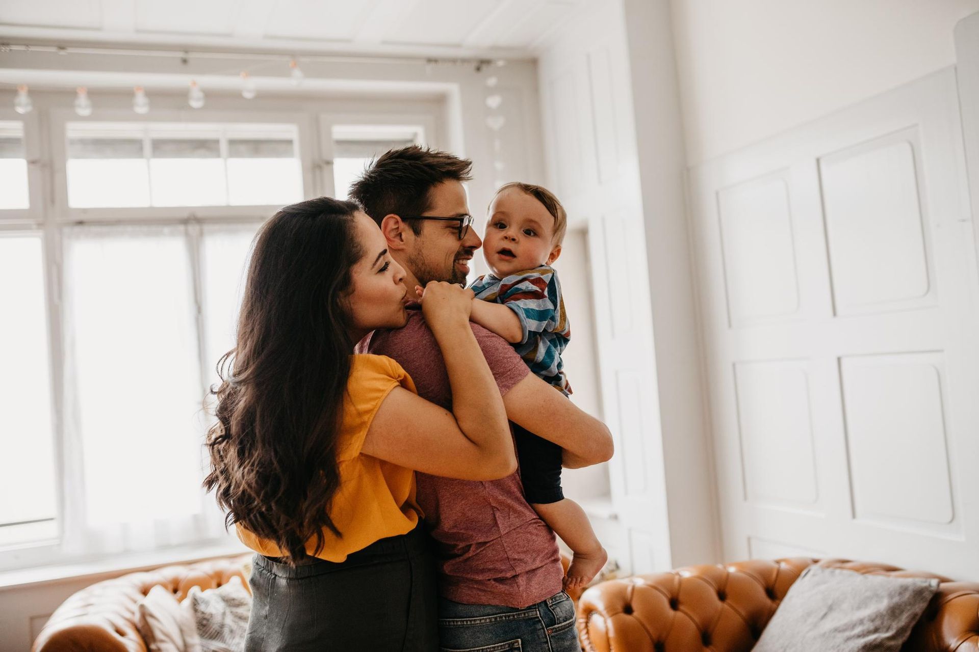 Adult holding a baby while standing by a bright window in a cozy living room