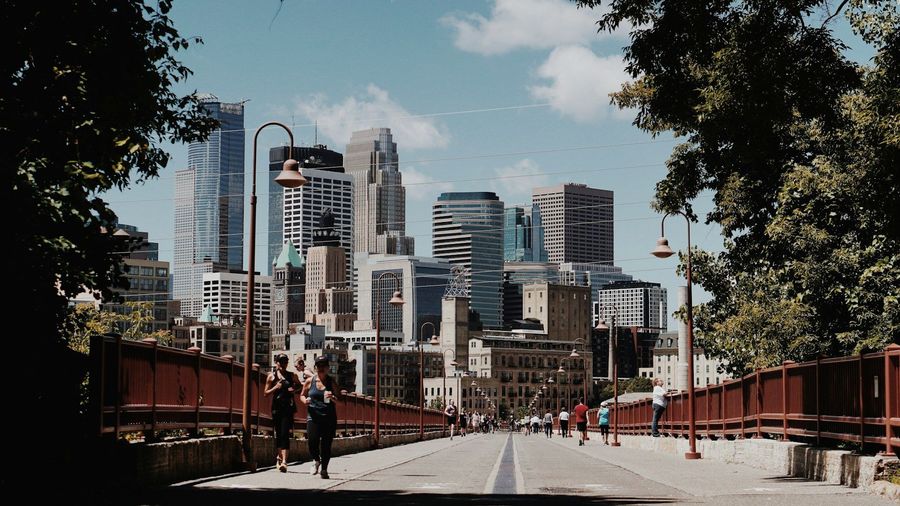 Pedestrian bridge leading toward a modern city skyline under a cloudy blue sky