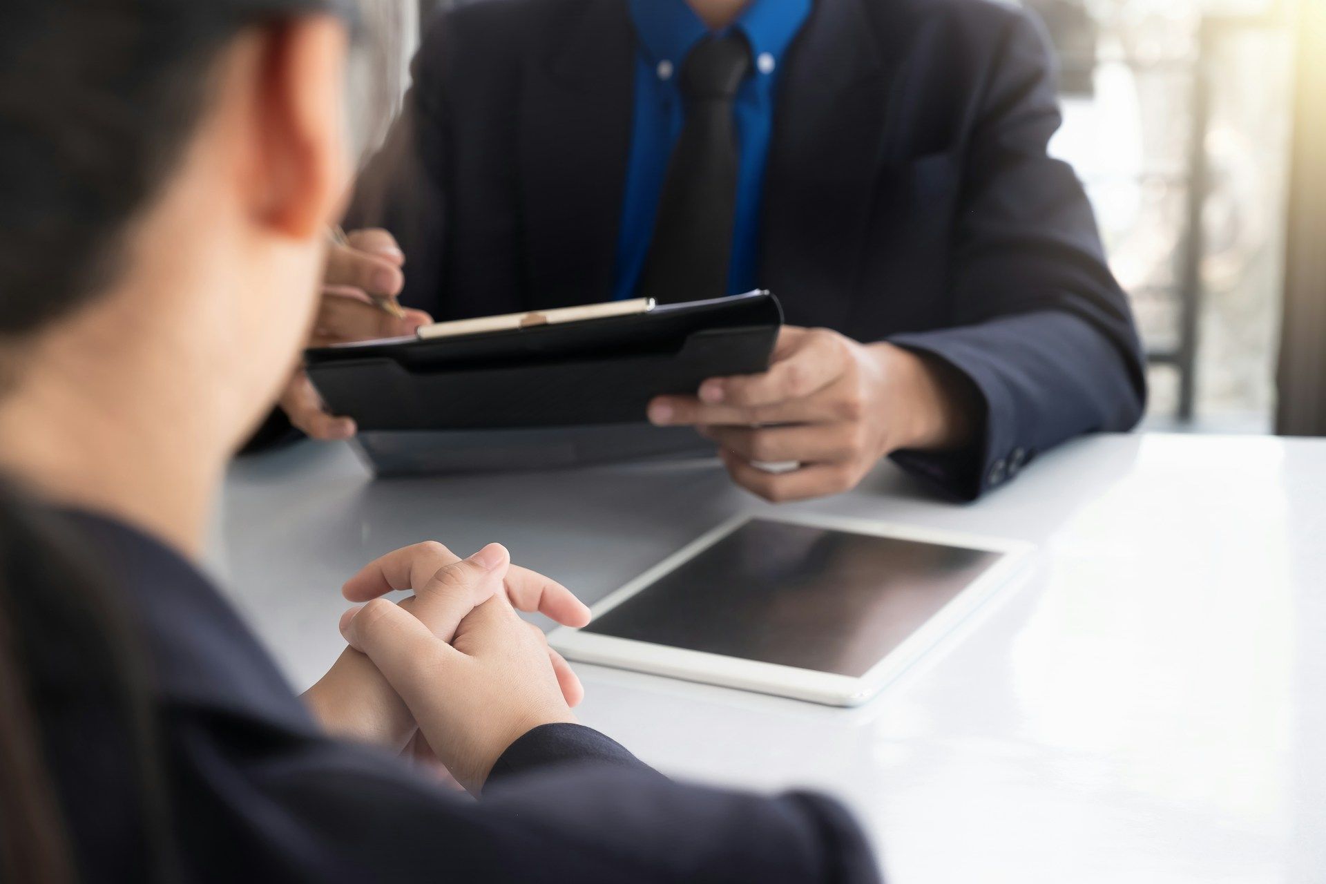 Two people in business attire discussing a tablet across a desk