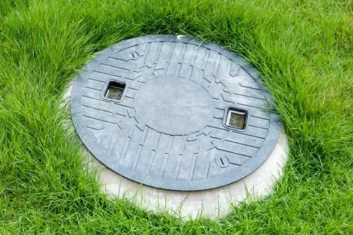 Round gray manhole cover in green grass with two square handles