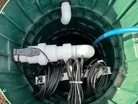 Green utility pit with bundled black cables and white conduit fittings inside a circular chamber