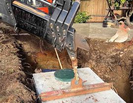 Excavator arm lifting a concrete slab over a muddy trench at a construction site