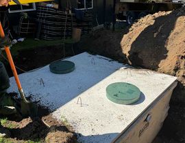 Outdoor septic tank with two green access covers beside a pile of dirt and a shovel.