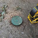 Round green utility cover in muddy ground beside a yellow cable reel.