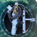 Coiled gray cable and white pipe attached to a metal bracket inside a green cylindrical chamber
