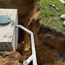 Septic tank beside a dug trench with white drainage pipes running into the ground.