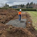Worker in orange vest leveling gravel in a long trench at a construction site