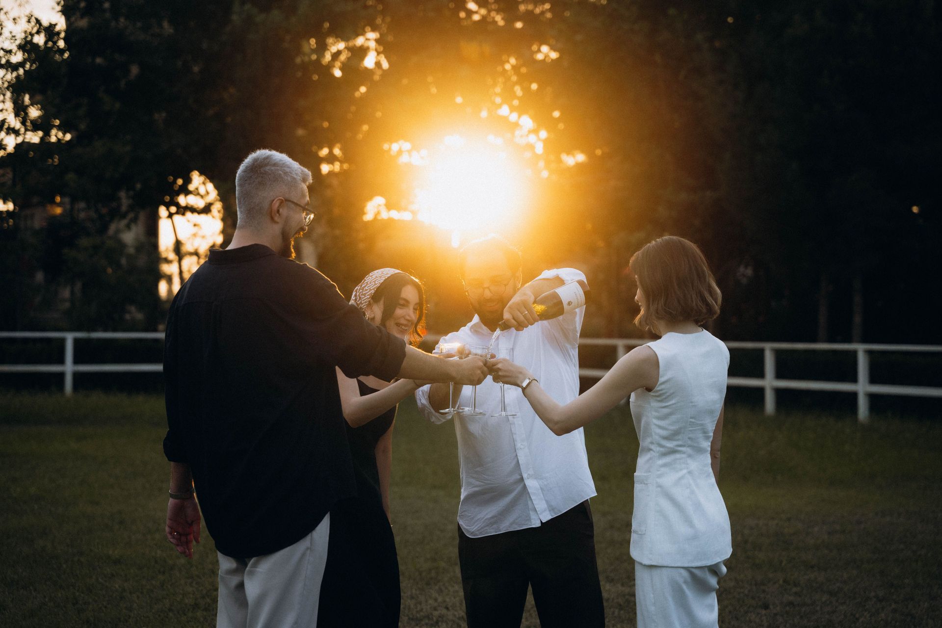 Four people standing in a circle outdoors at sunset, holding hands in a grassy field.