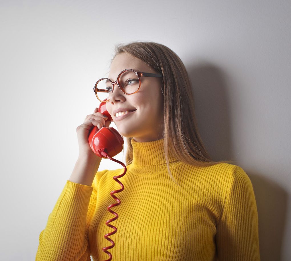 Woman in a yellow sweater smiling while holding a red corded phone to her ear