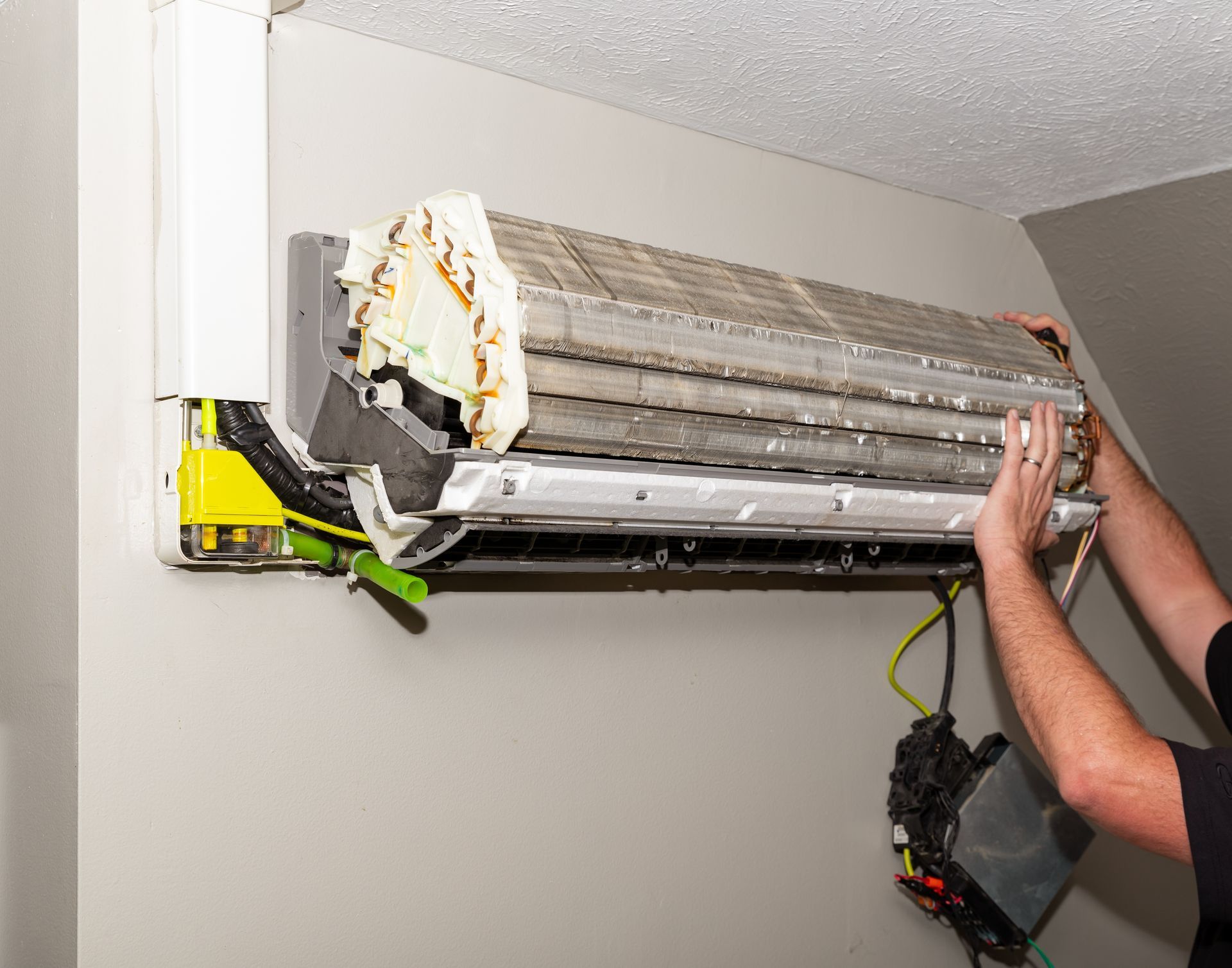 Wall-mounted air conditioner being removed, with exposed coils and a person’s hands supporting it