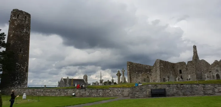 Ruins of a stone castle under cloudy skies, with a tall round tower and green grass in front.