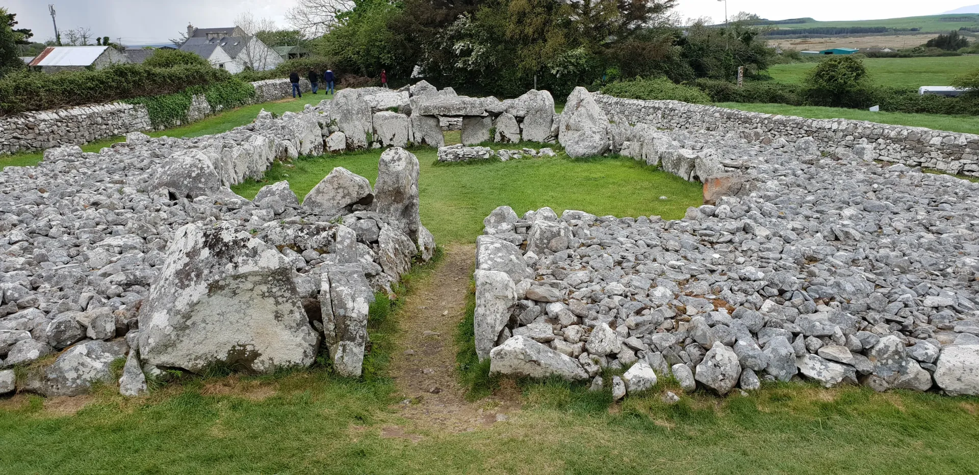 Stone ruins with low walls surrounding a grassy central enclosure in a rural landscape