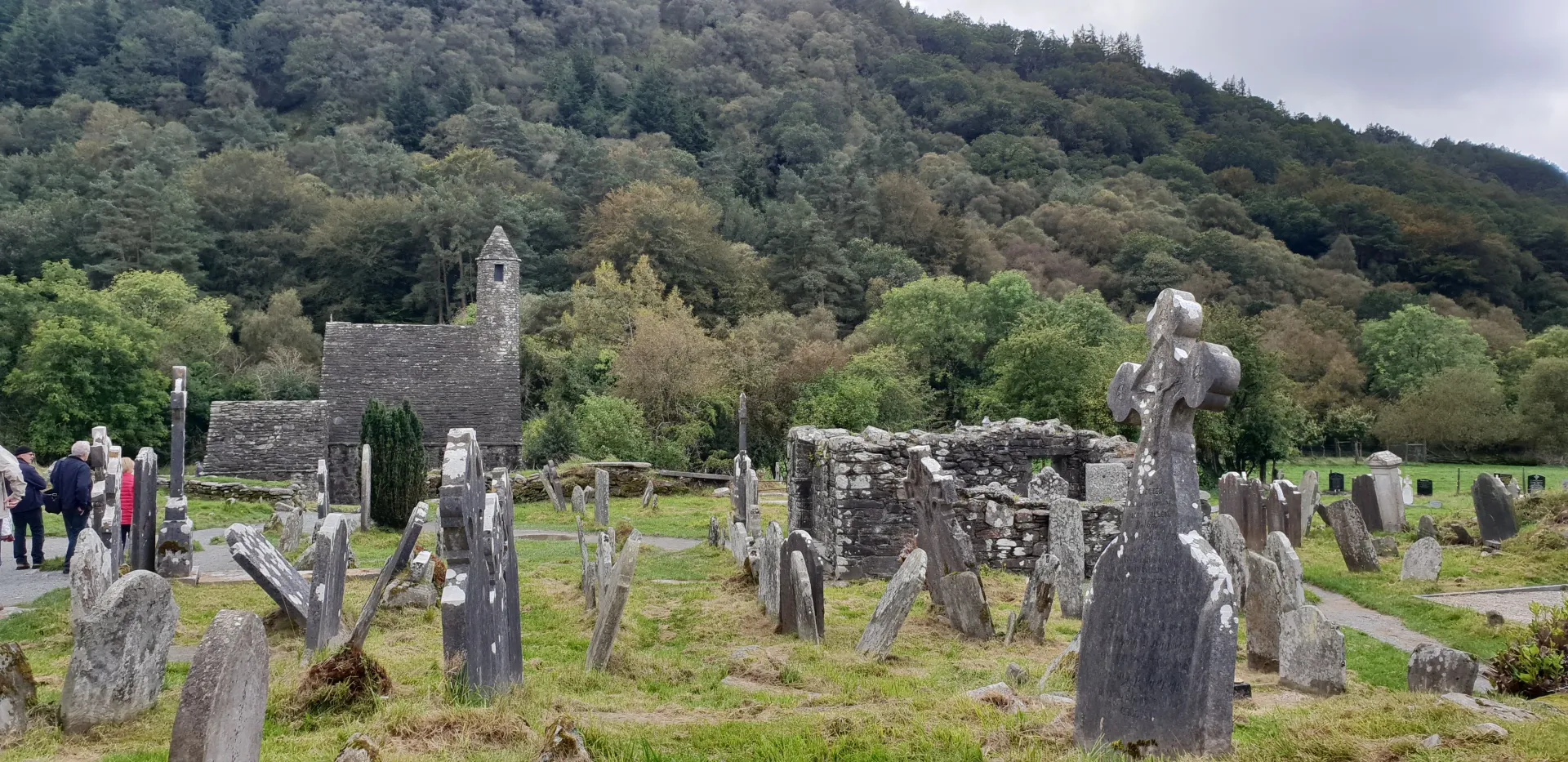 Ancient stone grave markers in a grassy cemetery with a wooded hillside behind them.
