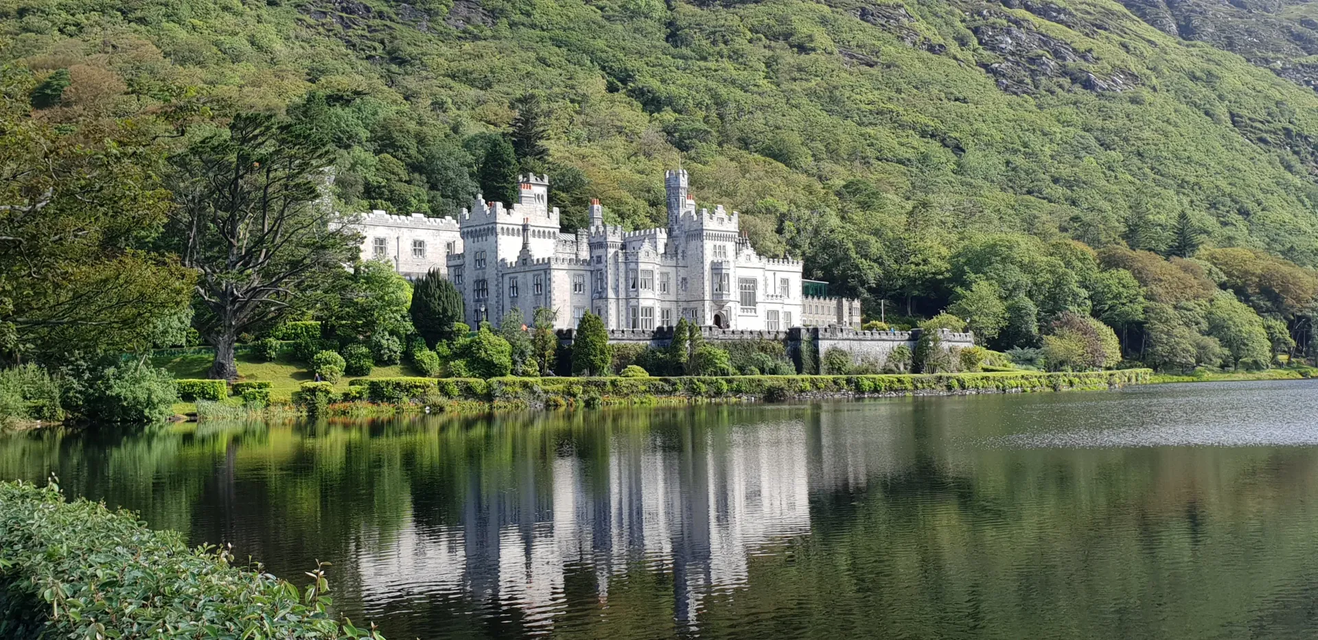 White lakeside castle reflected in calm water, backed by green forested hills