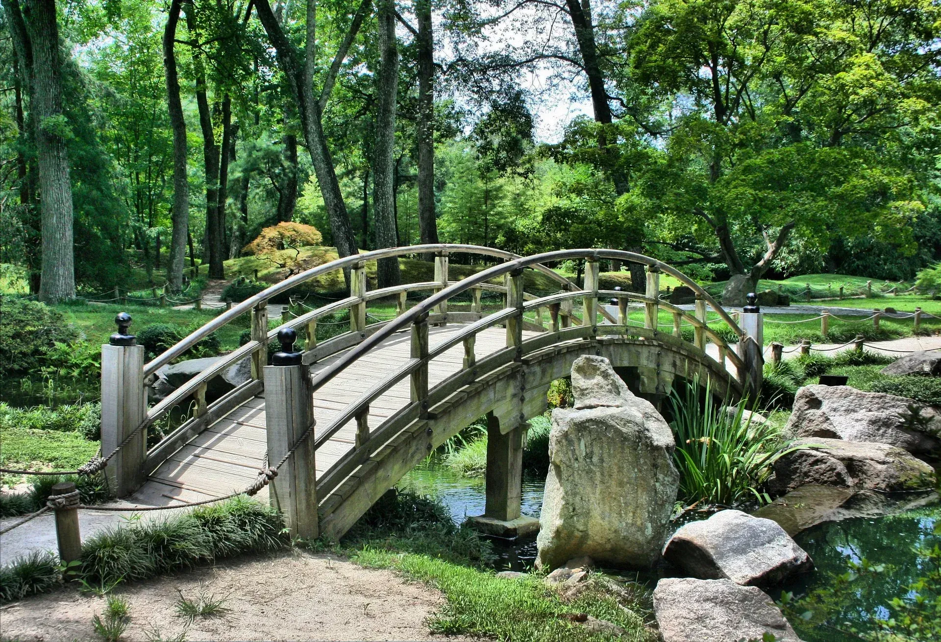 Wooden arched bridge over a small stream in a lush green garden park