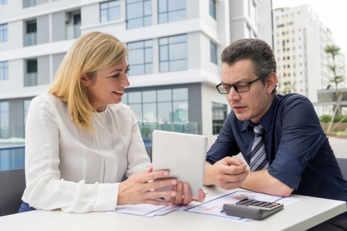 A man and a woman are sitting at a table looking at a tablet.