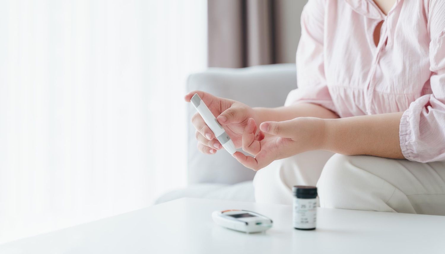 Woman testing blood sugar at home, holding a meter, sitting on a couch.