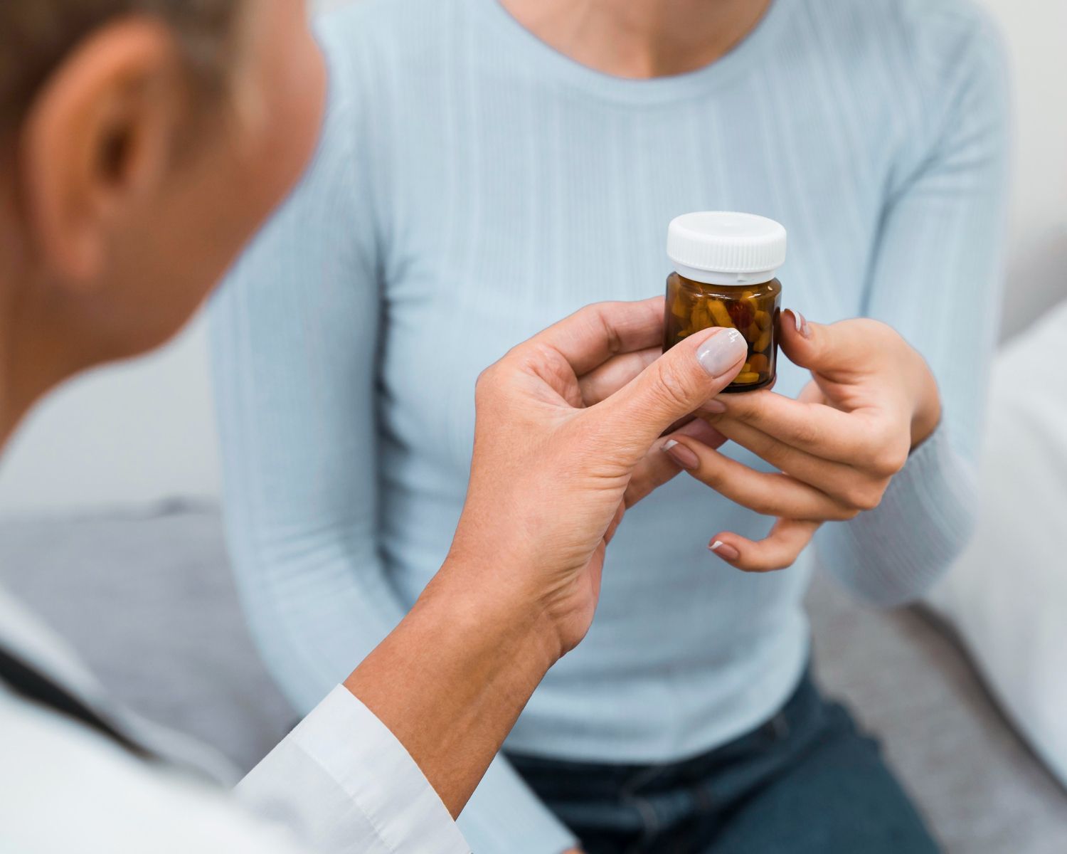Doctor handing a pill bottle to a patient in an examination room.