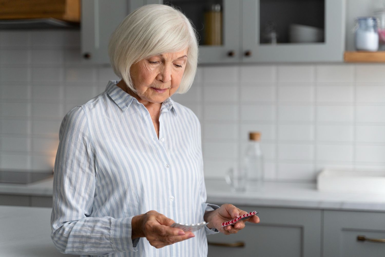 Older woman in kitchen holding pills, preparing to take medication.