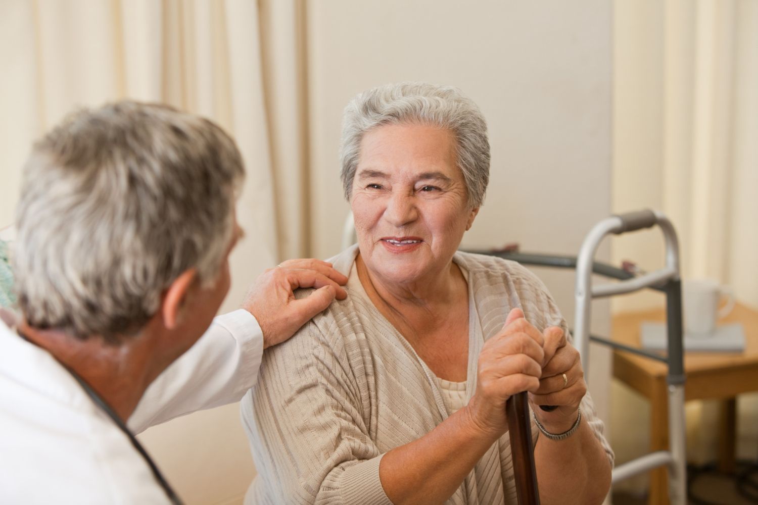 Doctor comforts elderly woman with cane; indoor setting, gentle smiles.