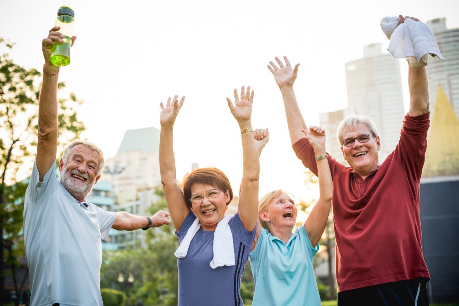 Four active seniors with arms raised in victory outdoors; sunny park.