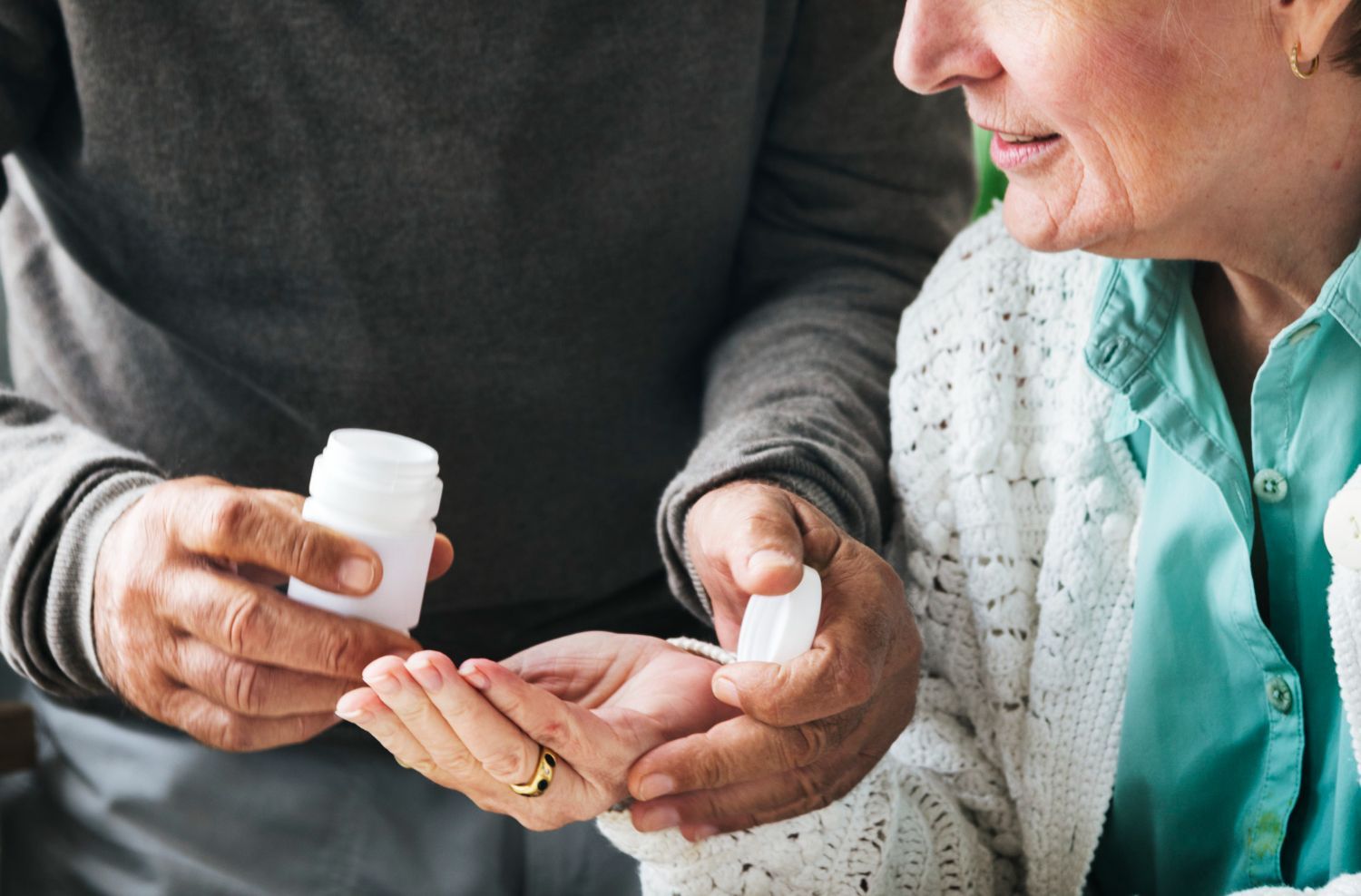 Person giving pills from a white bottle to an elderly woman.