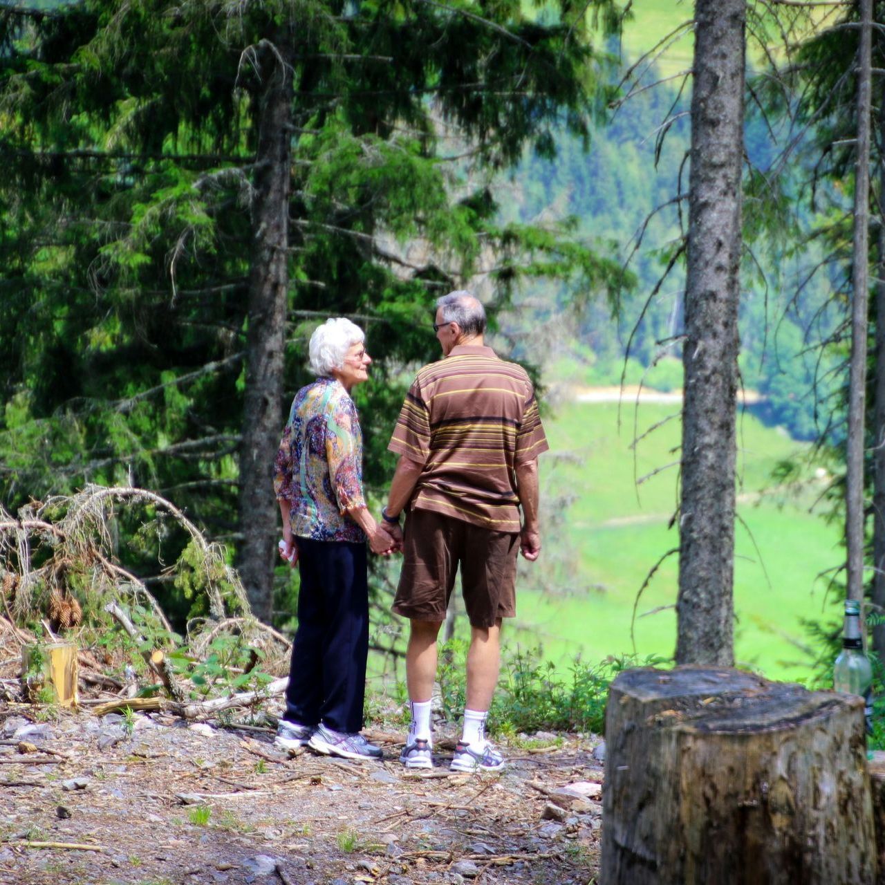 A man and a woman are standing in the woods holding hands