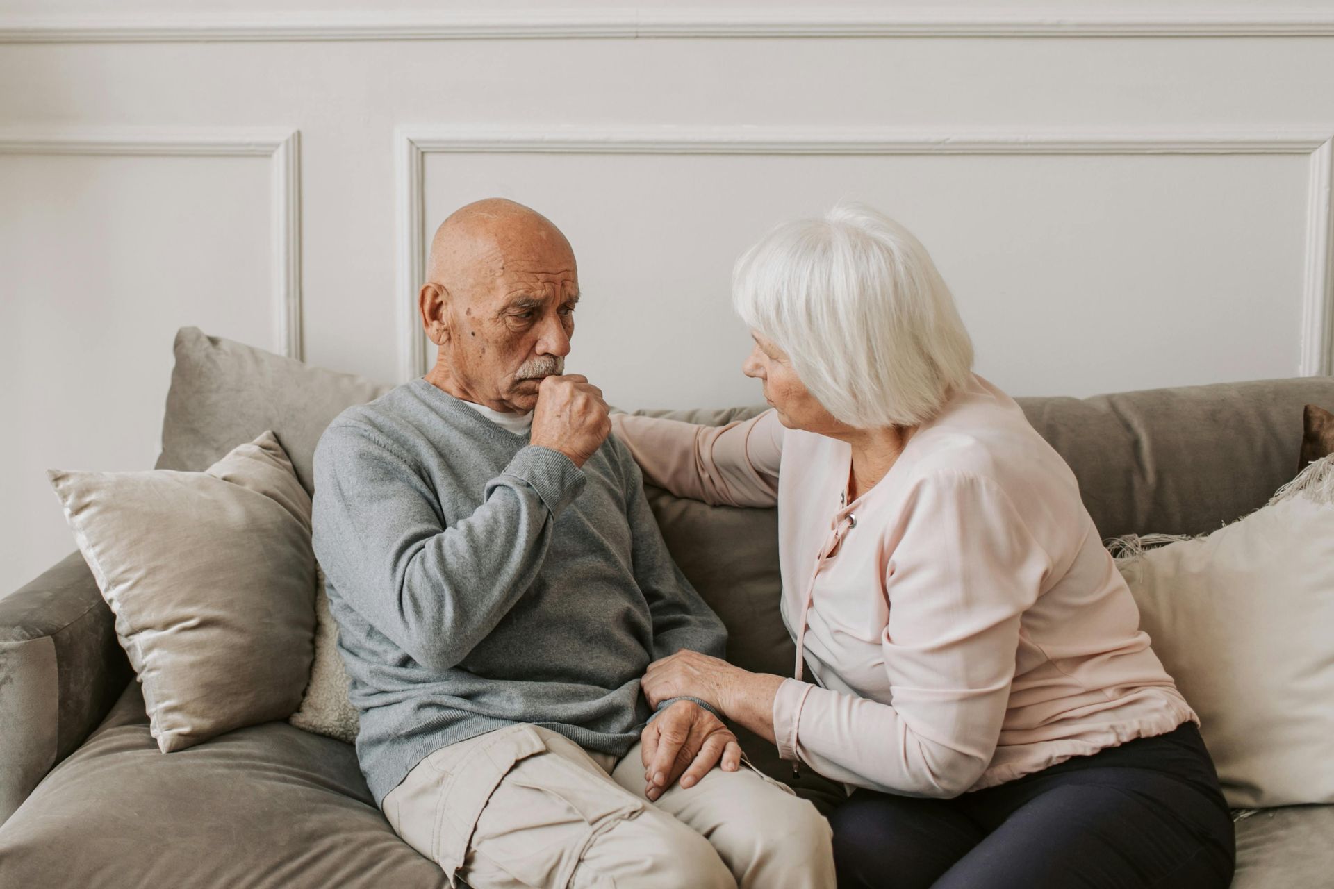 An elderly couple is sitting on a couch talking to each other.