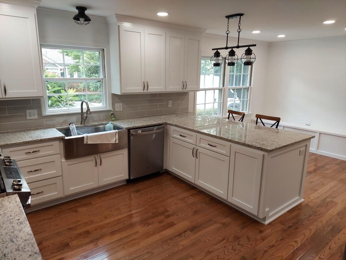A brightly lit kitchen with white cabinets, granite countertops, stainless steel appliances, and wood flooring.
