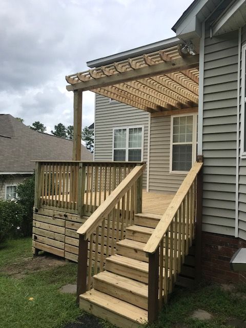 A new wooden deck and pergola attached to the back of a house with steps leading down to a grassy yard.