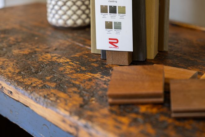 Piano di un tavolo in legno con un campionario di finiture e un campione di legno su una superficie rustica e usurata.