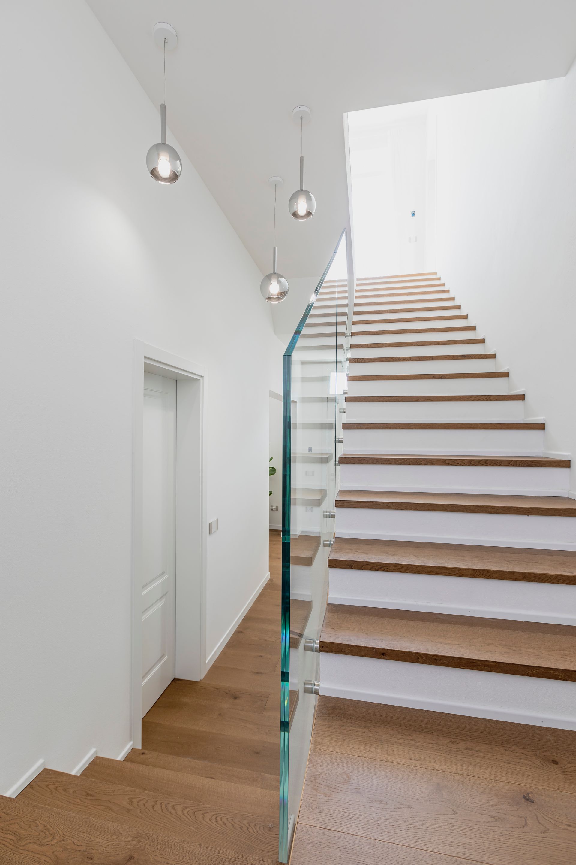 Scala moderna in legno con ringhiera in vetro in un luminoso corridoio interno bianco