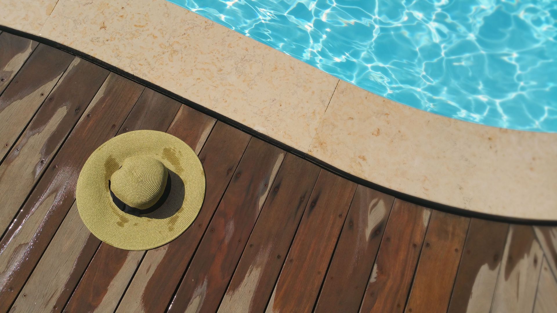 Cappello di paglia sul bordo piscina in legno accanto all'acqua blu del nuoto
