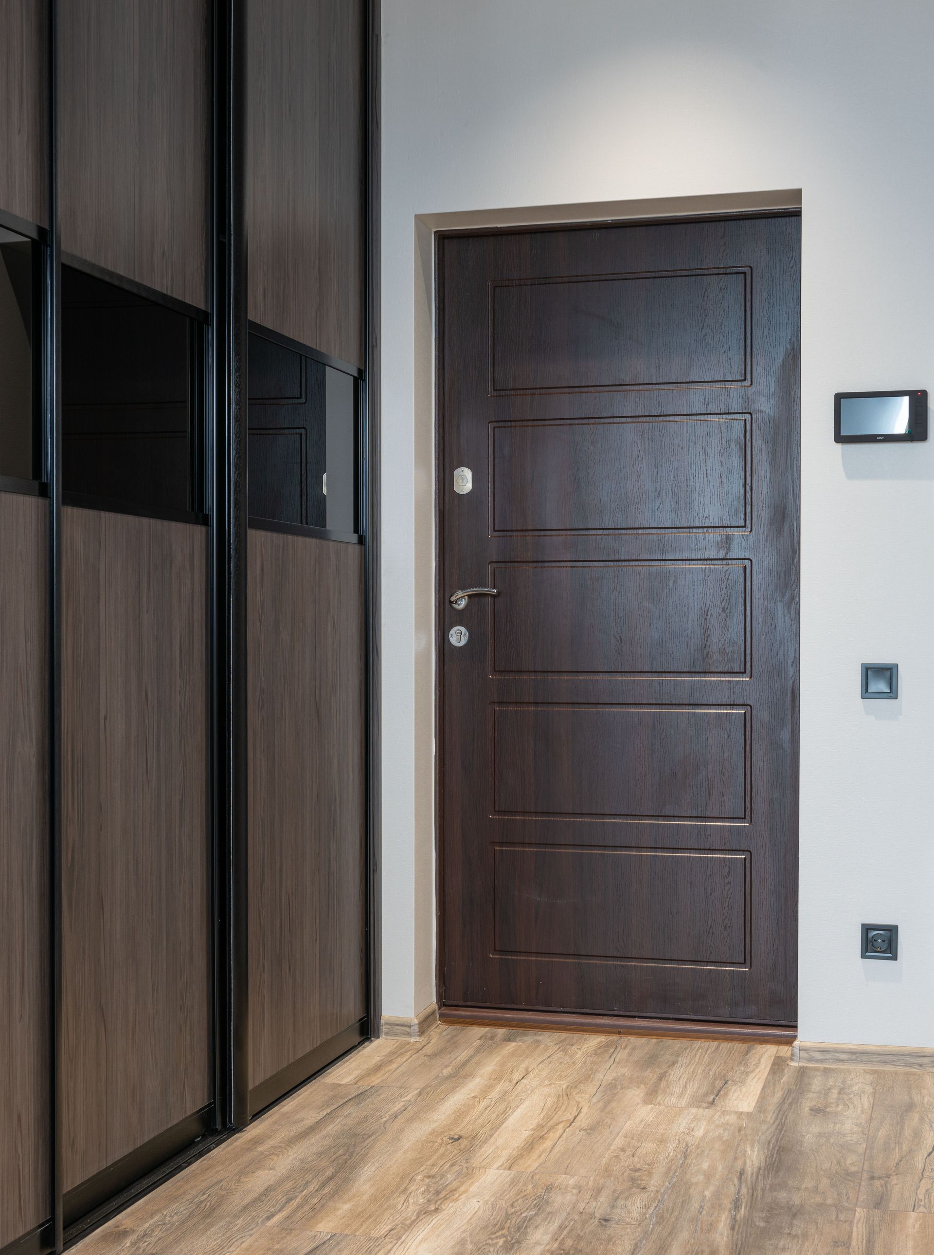 Ingresso moderno con porta in legno scuro, armadi a muro e pavimento in legno chiaro.