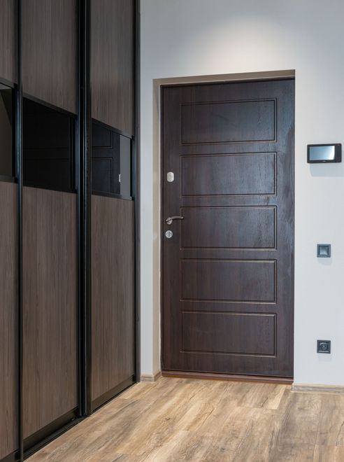 Ingresso moderno con porta in legno scuro, armadi a muro e pavimento in legno chiaro.