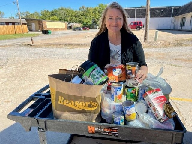 A community food bank van parked outdoors next to a rolling cart filled with bags of food.