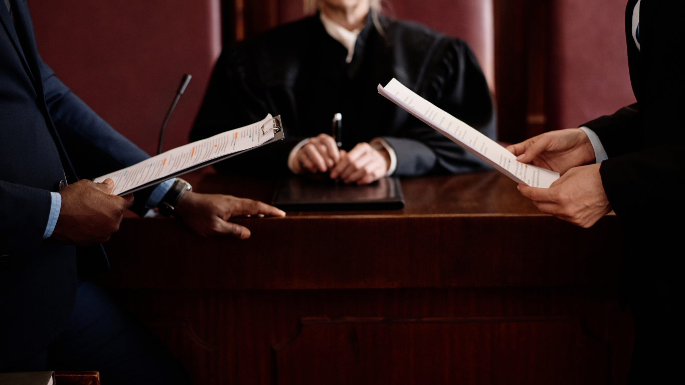 Two people holding pens across a conference table, suggesting a contract signing discussion
