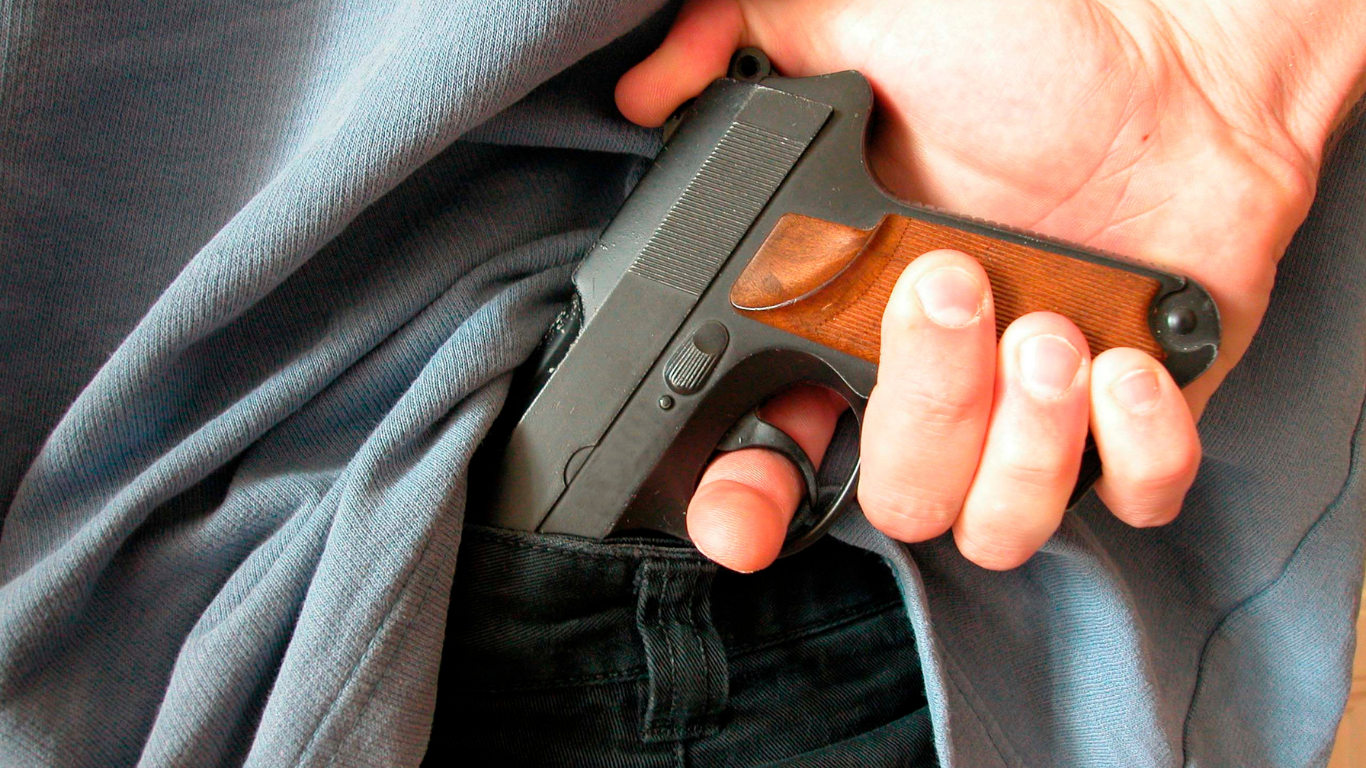 A hand grips a black handgun tucked into a waistband under a gray shirt.