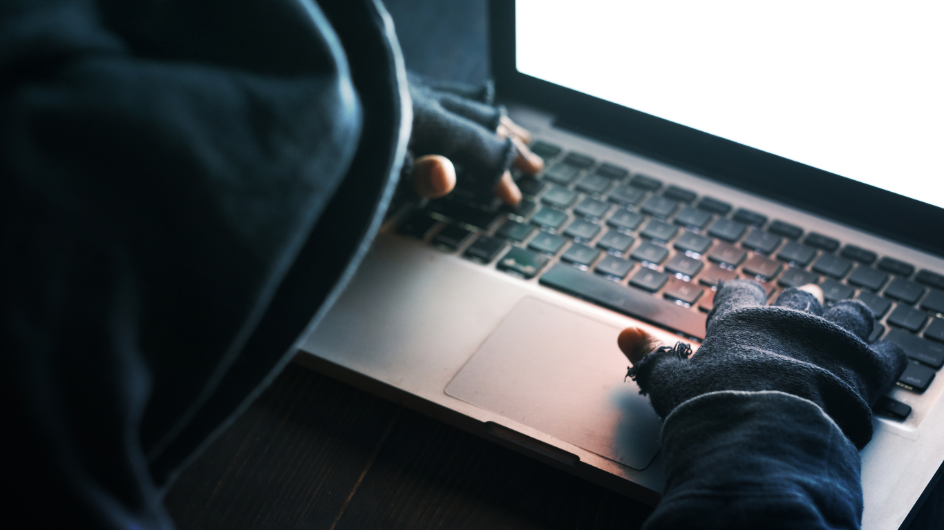 Gloved hands typing on a laptop keyboard in a dimly lit setting
