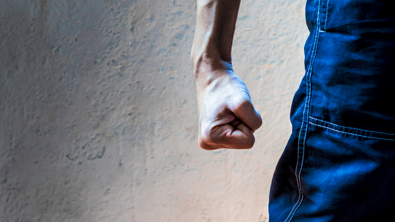 Clenched fist beside a person in blue jeans against a plain wall