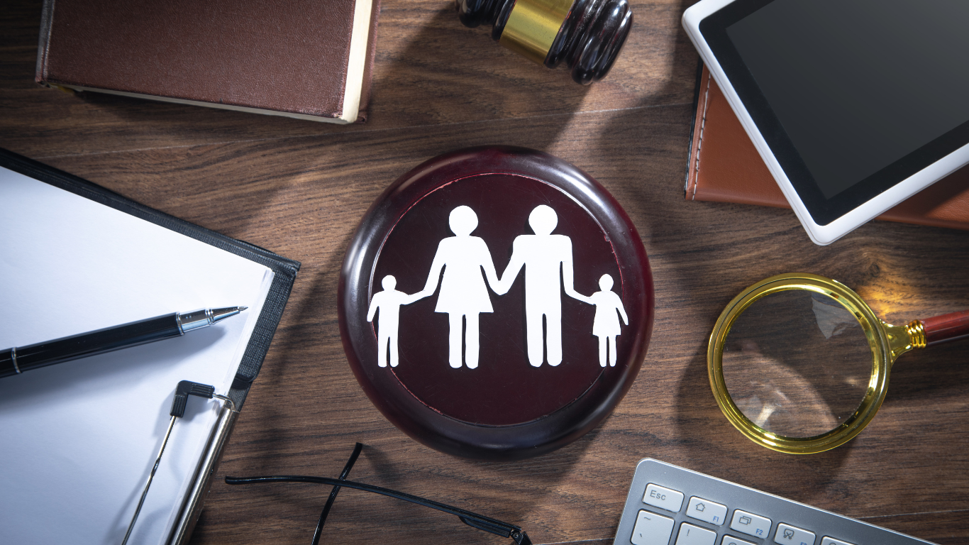 Family silhouette icon in a dark circular button on a desk with tablet, magnifying glass, and keyboard