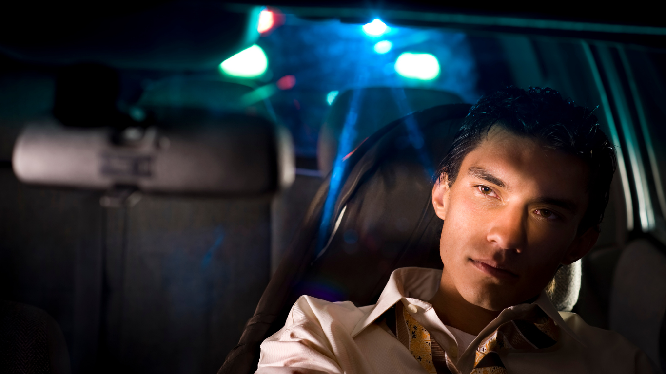 Man sitting in a car at night, lit by blue and red dashboard lights, looking thoughtfully ahead