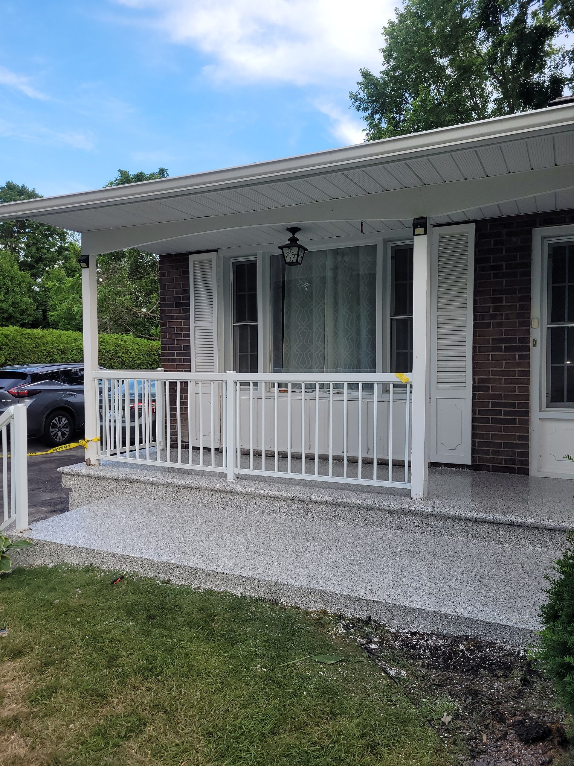 Front porch with white railing and awning on a brick house, bordered by gravel and lawn.