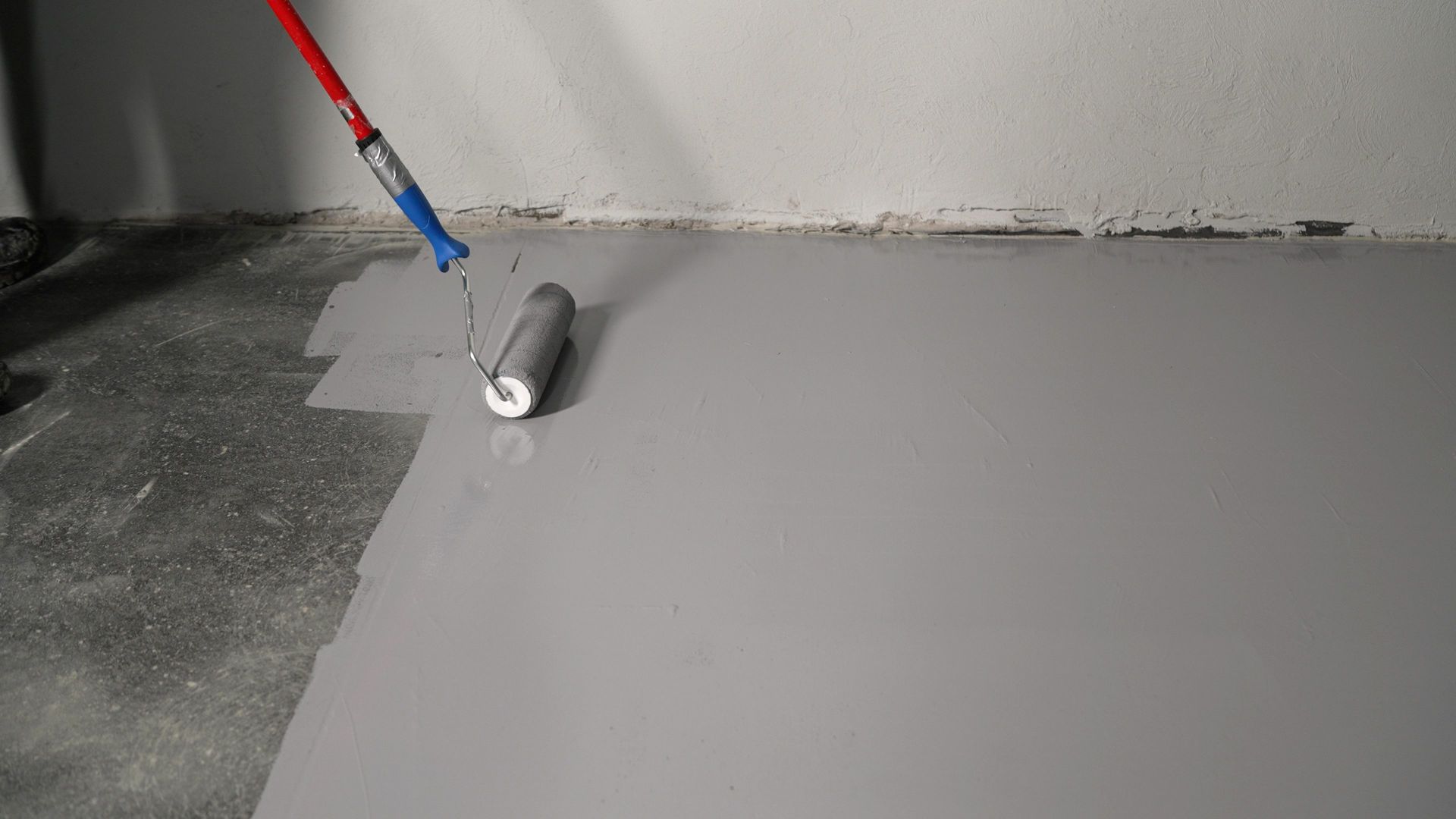 A person is painting a concrete floor with a roller.